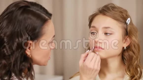 化妆师在客户脸上化妆在女孩的嘴唇上涂上油漆视频的预览图