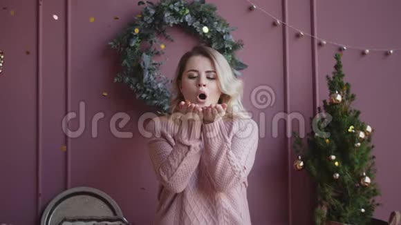 穿着毛衣的漂亮女人用手慢慢地把闪亮的纸屑吹向相机圣诞气氛视频的预览图