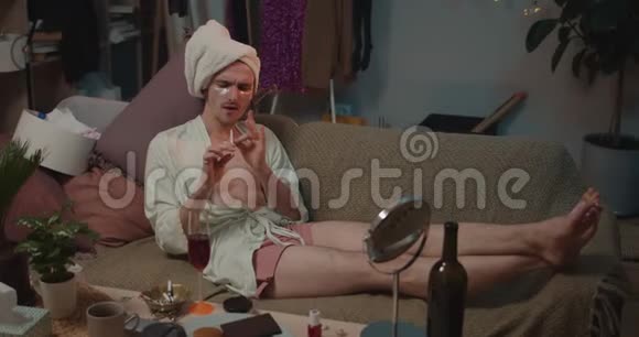 穿着缎子长袍的变性人在沙发上放松在听音乐时做美容程序青年变性人视频的预览图
