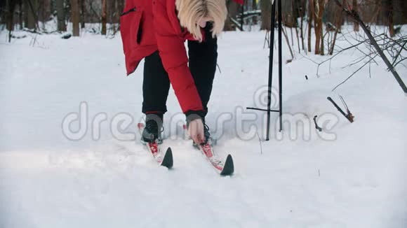 一位年轻的金发女子穿着红色羽绒服从滑雪场脱下靴子视频的预览图