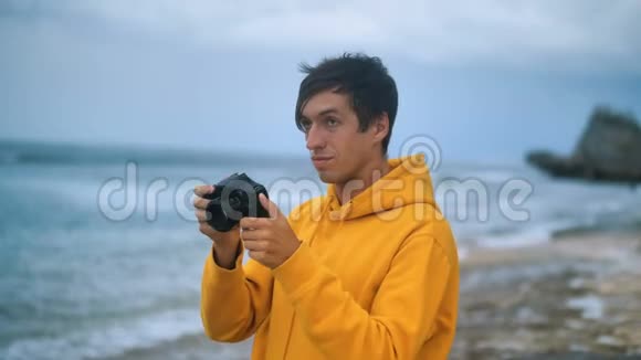傍晚一位身穿黄色连帽衫的摄影师在美丽的热带海滩上拍照视频的预览图