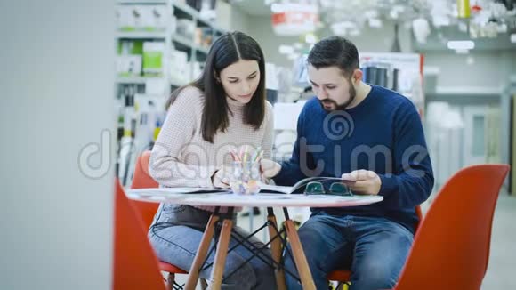 年轻夫妇坐在超市的一张桌子旁正在研究商品目录视频的预览图