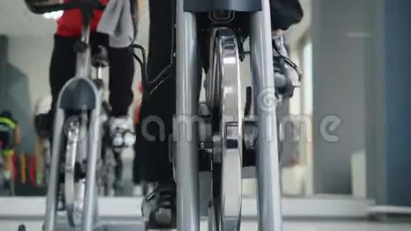 体育人士在健身俱乐部前景的自行车课上旋转脚踏车室内自行车男子和妇女训练自行车运动视频的预览图