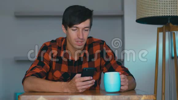 快乐的年轻人正在使用智能手机在家喝茶或咖啡在社交媒体上放松视频的预览图