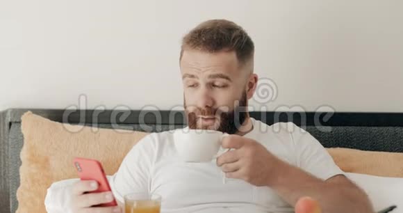 近距离观看英俊的胡须男人在床上喝咖啡微笑着对客米娅三十年代快乐男人的画像视频的预览图