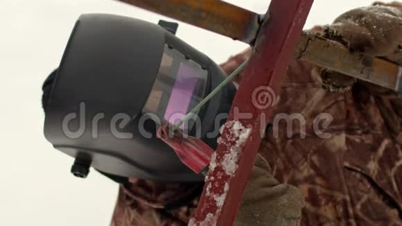 一名蒙面男性焊工正在焊接金属型材一个穿着冬季工作服和焊接面罩的人用焊接工作视频的预览图