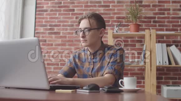 一个穿鼻子的年轻潮人正在笔记本电脑上打字脸上带着微笑转向相机自由职业者视频的预览图