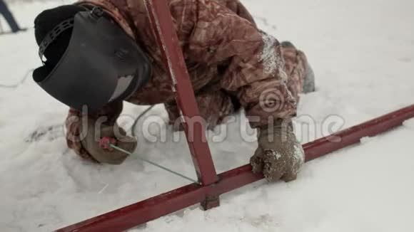 一名焊工在雪中跪着焊接金属框架的特写穿着冬装手套和电焊面罩的人视频的预览图