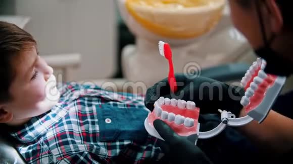 一个正在牙科治疗的小男孩用下巴模型来解释卫生的重要性视频的预览图