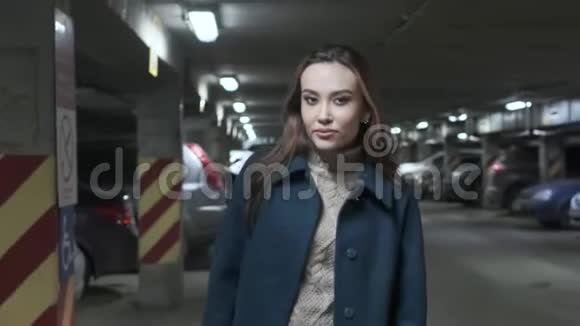 穿着外套的时髦微笑可爱的亚洲女孩沿着汽车在地下停车场散步视频的预览图
