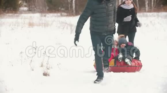 一家人在森林附近的户外跑步男人把他的孩子卷在充气雪橇上视频的预览图