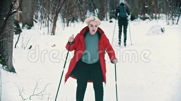 一位身穿红羽绒服的年轻金发女子在森林里滑雪冬季活动视频的预览图
