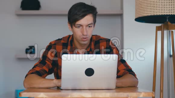兴奋不已的年轻人自由职业者看着笔记本电脑庆祝在家工作的成功视频的预览图