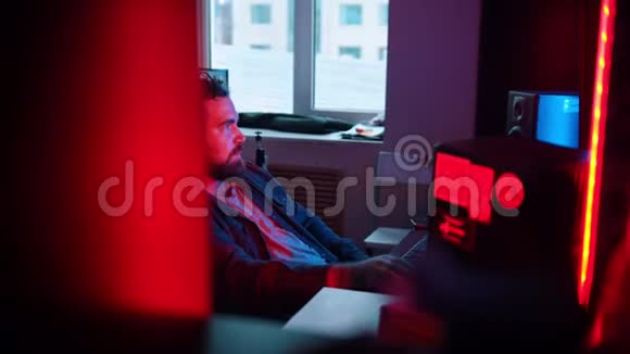 一位留胡子的音响工程师戴着耳机坐在录音室里正在做这个项目视频的预览图