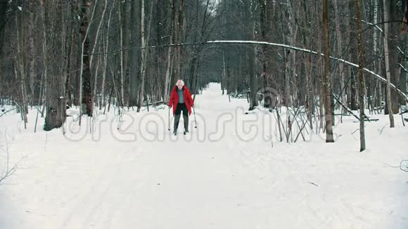 一位年轻的金发女郎穿着红色羽绒服在树林里努力滑雪视频的预览图