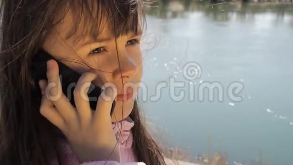 河边带手机的孩子那个女孩正在新鲜空气中打电话春天阳光明媚的一天视频的预览图