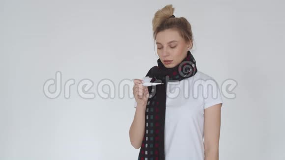 一个生病的女孩看着温度计和戴上医疗面具的肖像一个戴着围巾的生病女孩视频的预览图