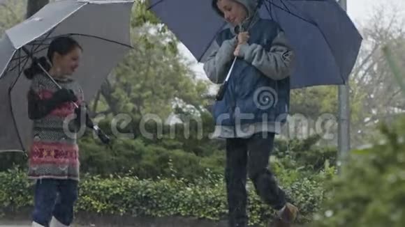 男孩和女孩带着雨伞在倾盆大雨中缓慢地跳跃视频的预览图