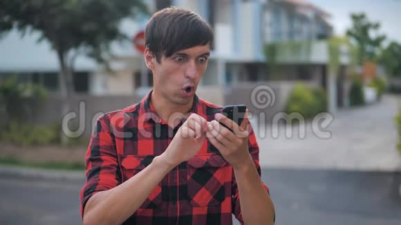 害怕的年轻人被他在智能手机上看到的东西震惊了站在城外的街道上震惊男性阅读不良视频的预览图