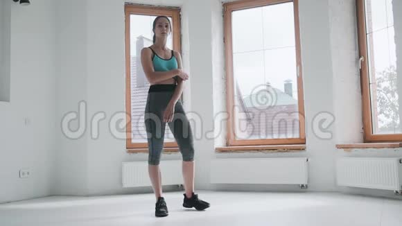 穿着运动服的漂亮女孩站在家里明亮的房间里视频的预览图