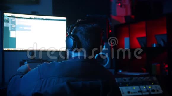 一位戴耳机的男声工程师在霓虹灯录音室工作视频的预览图