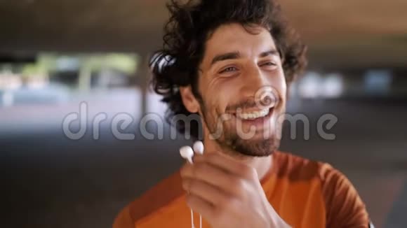 一位微笑的运动员年轻男子在户外用白色耳机听音乐的肖像视频的预览图