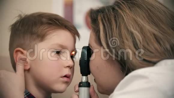 一个正在眼科诊所接受治疗的男孩一位女医生用一种明亮的设备检查小男孩视力视频的预览图
