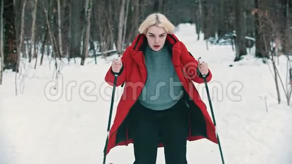 一位年轻的金发女郎穿着红色羽绒服在森林里努力滑雪视频的预览图