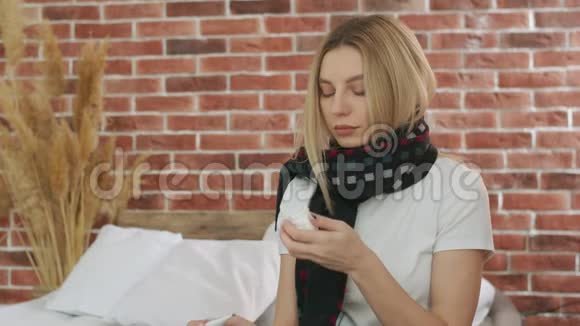 一个带着围巾的生病女孩用纸手帕擦鼻涕看着体温计叹了口气视频的预览图