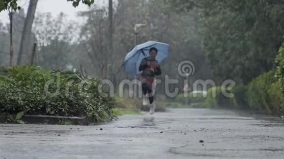 一个小女孩在雨中撑着伞在水坑里跳跃的慢动作视频的预览图