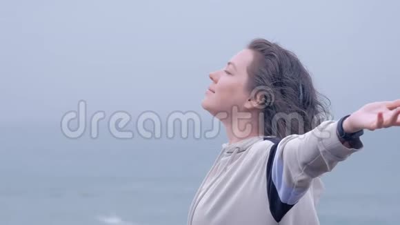 一个蓝眼睛的女人在海滩上灰色雨天下雨的肖像视频的预览图