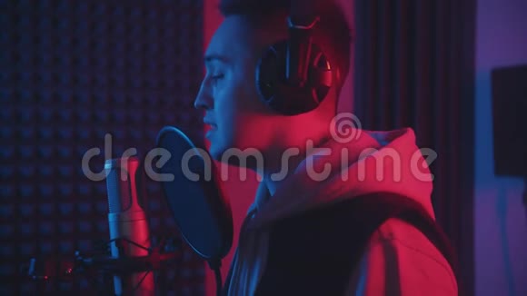 一个戴着耳机的男人在麦克风里的弹出式滤镜里唱着歌霓虹灯中的录音室视频的预览图