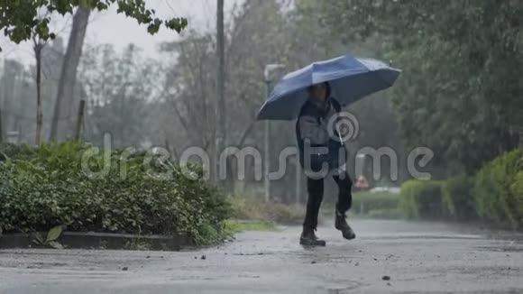 一个小男孩拿着雨伞在倾盆大雨中跳跃的缓慢动作视频的预览图