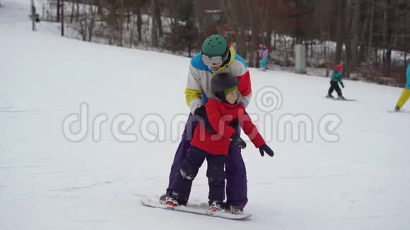 年轻人滑雪板教练教小男孩如何骑滑雪板冬季活动概念视频的预览图