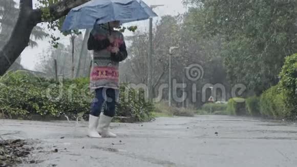 一个小女孩在雨中撑着伞在水坑里跳跃的慢动作视频的预览图