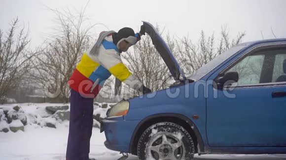 冬天下着雪路上的人汽车出毛病了他正试图找出引擎的问题视频的预览图