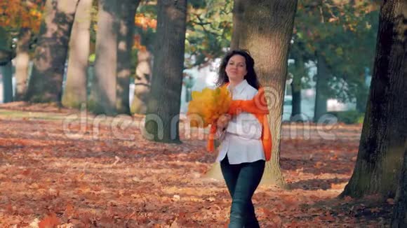 在公园里一个年轻的女人带着一束黄色的秋叶享受着落叶视频的预览图