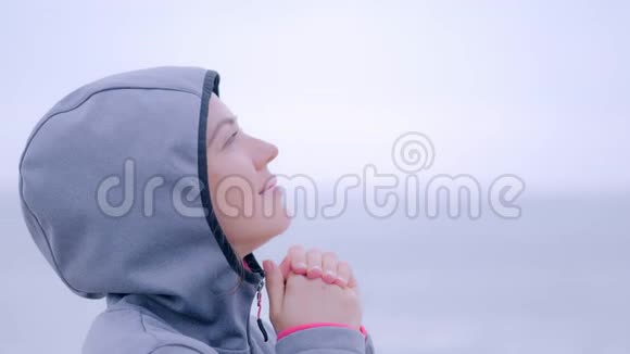 在灰蒙蒙的沙滩上祈祷穿雨衣的女人视频的预览图