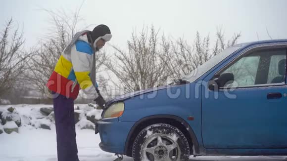 冬天下着雪路上的人汽车出毛病了他正试图找出引擎的问题视频的预览图