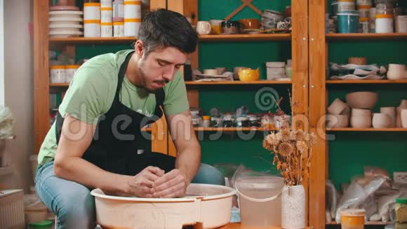 陶器主人正在用一桶水润湿他的手并继续用粘土工作视频的预览图