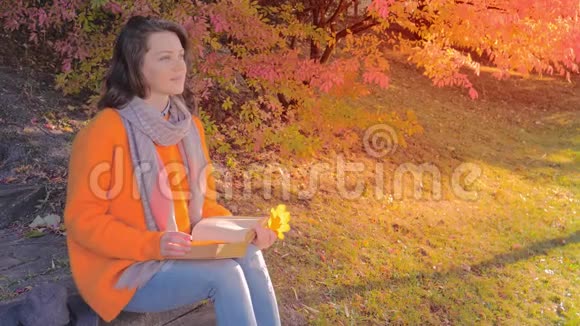 美丽的女人在秋天的花园里看书坐在台阶上视频的预览图