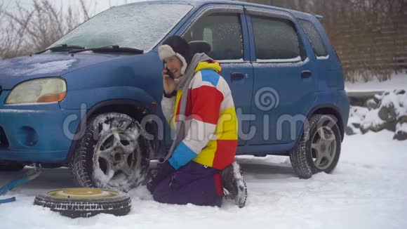 冬天下着雪路上的人汽车出毛病了他正试图更换车轮但他不能视频的预览图