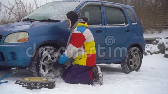 冬天下着雪路上的人汽车出毛病了他正试图更换车轮但他不能视频的预览图