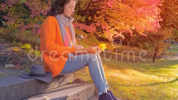 美丽的女孩在台阶上的秋天花园里休息和看书视频的预览图