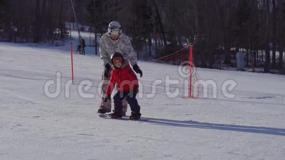 年轻人滑雪板教练教小男孩如何骑滑雪板冬季活动概念视频的预览图