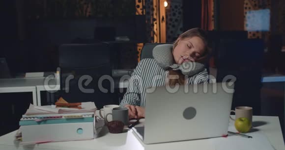 年轻的过度劳累的女人在打开的笔记本电脑前坐在办公桌前睡觉女孩办公室经理累了视频的预览图