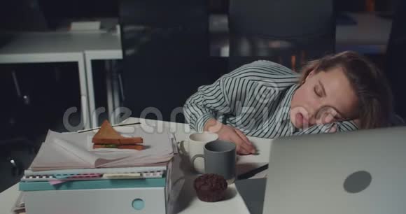 昏昏欲睡的年轻女性办公室工作人员躺在乱七八糟的桌子上面前有打开的笔记本疲倦的女人睡觉视频的预览图