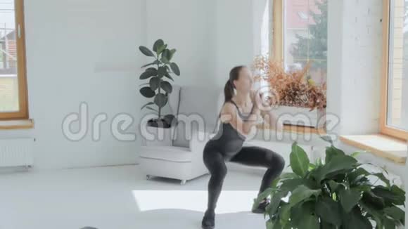 穿运动服的年轻黑发女孩在家做运动做蹲坐视频的预览图