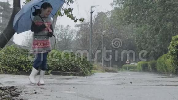 一个小女孩在雨中撑着伞在水坑里跳跃的慢动作视频的预览图