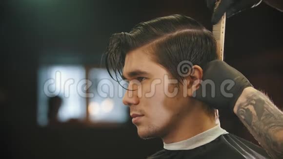 一个年轻男子在理发店理发时被纹身的理发师戴着黑色手套视频的预览图